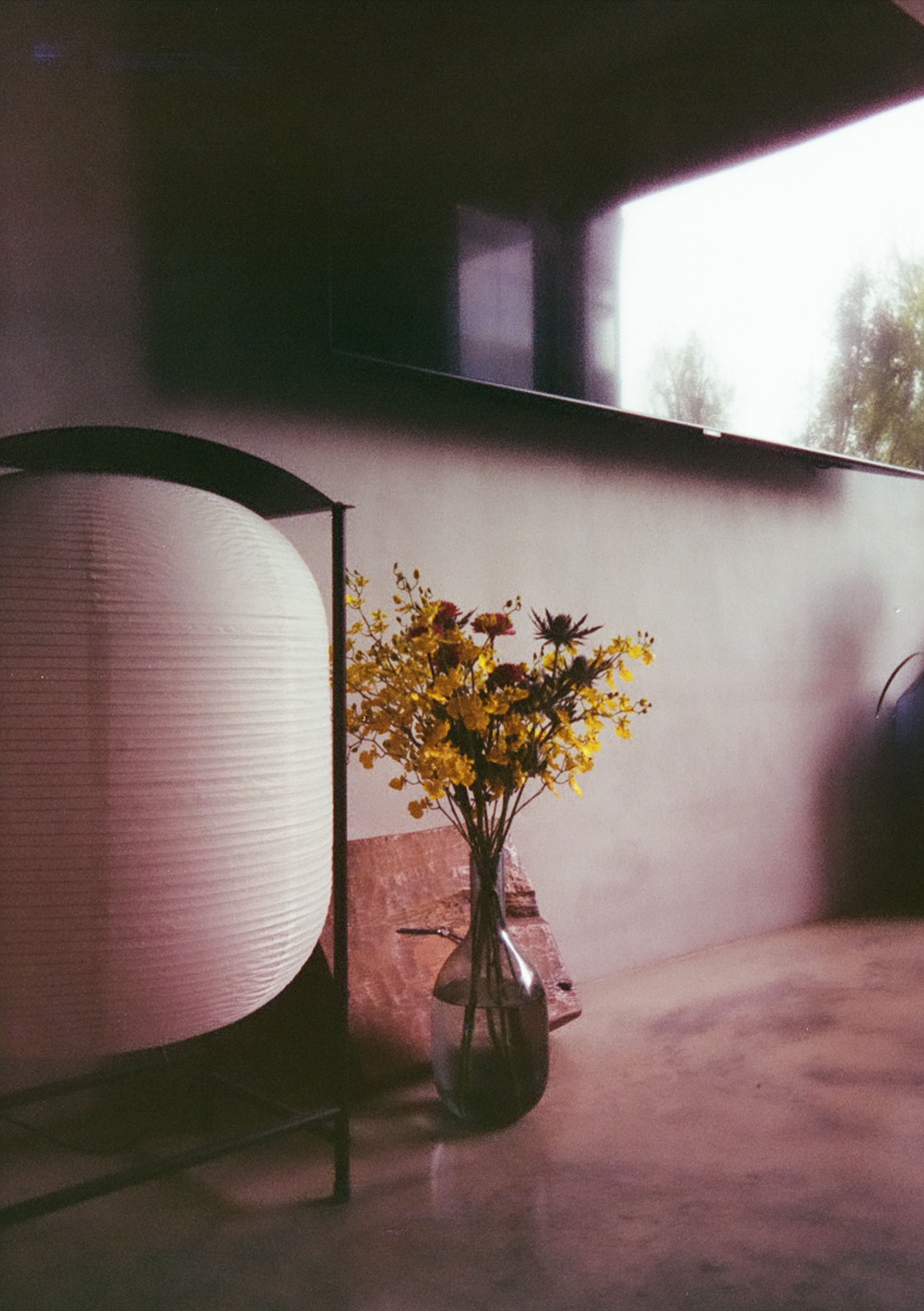 A floor lantern and a vase with yellow, purple, pink flowers. A TV on the wall.