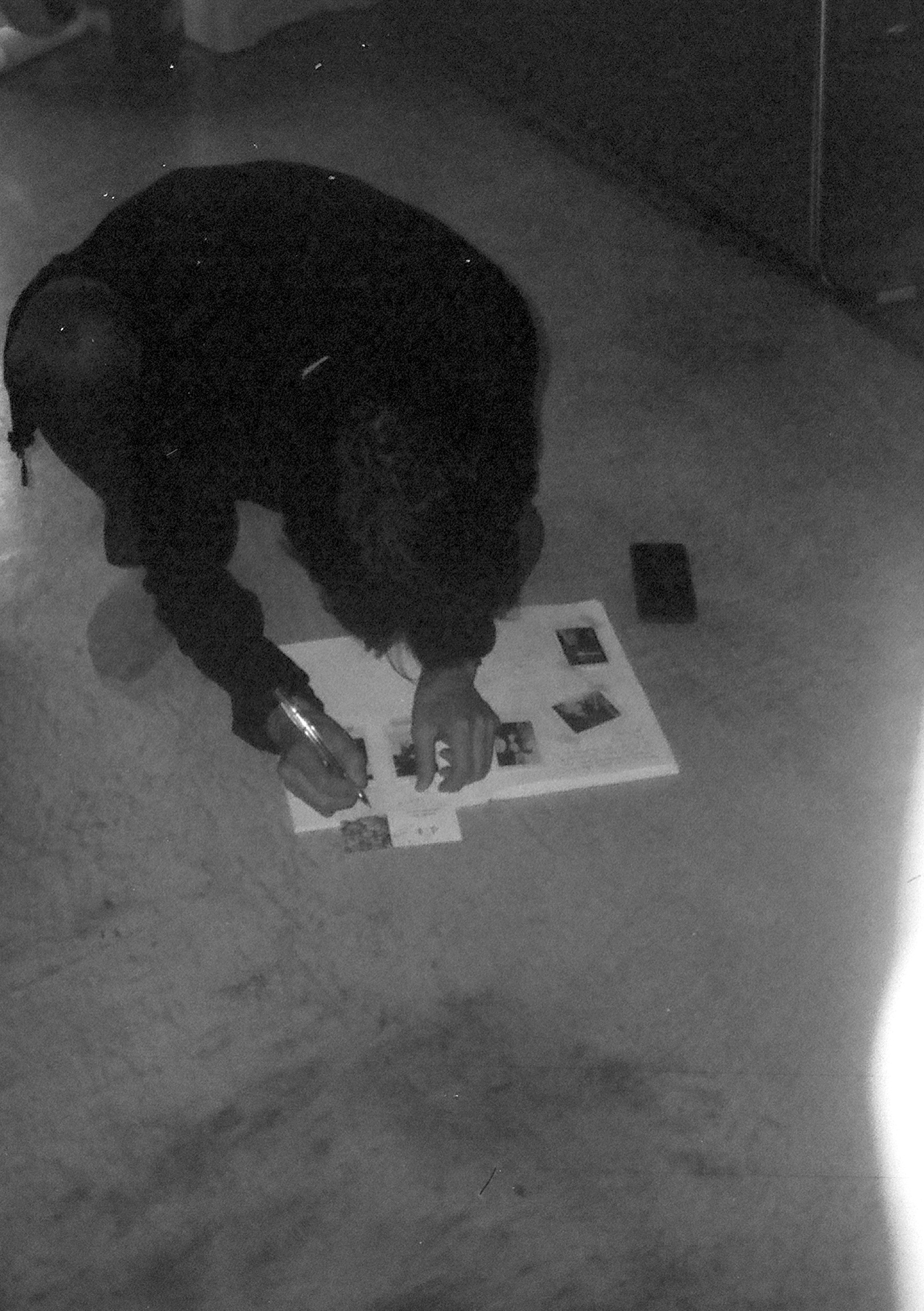 Man squatting down and writing on a book on the floor.