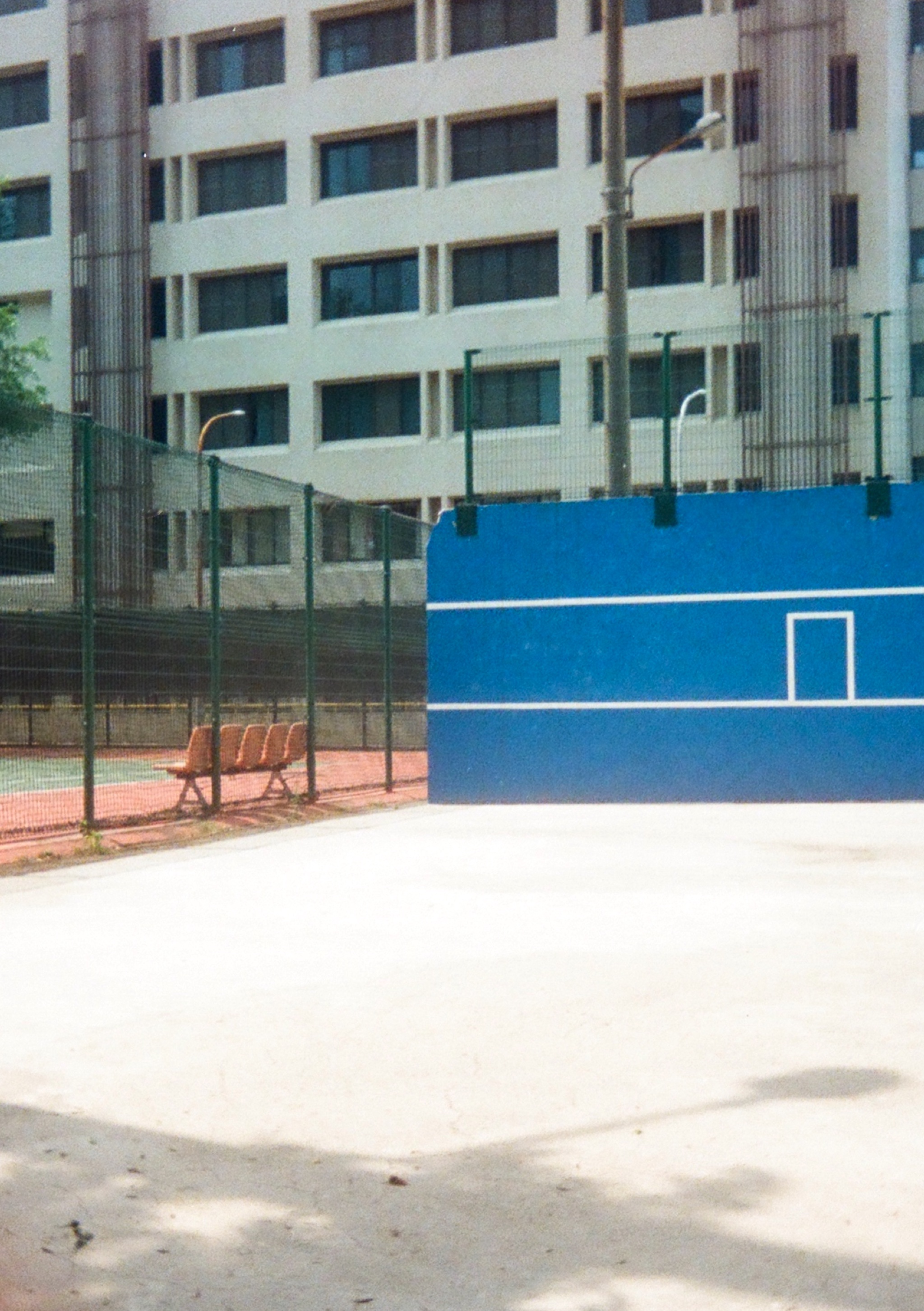 On a sunny day, a bright blue tennis wall, and a tennis court across a fence.