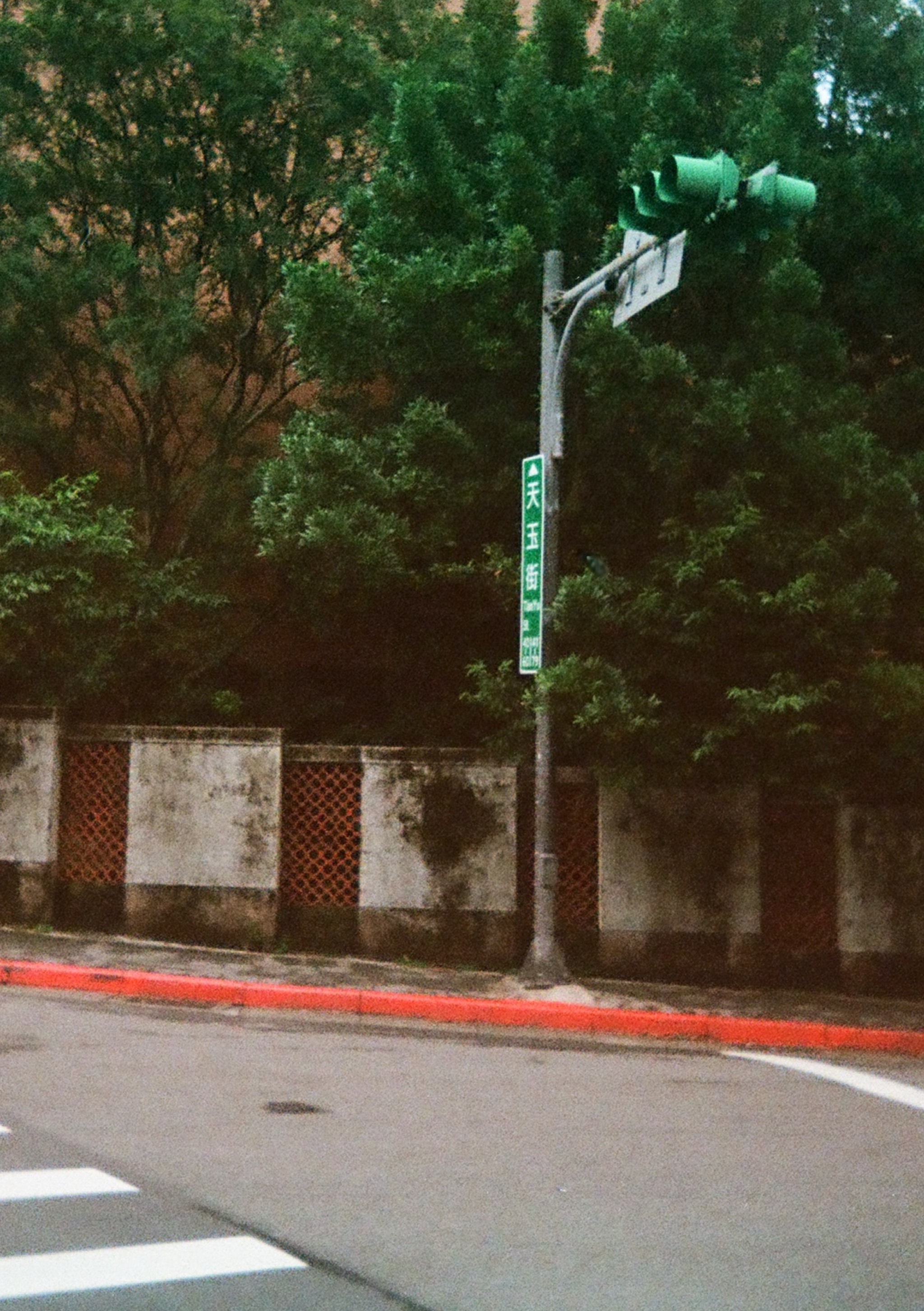 Trees inside of a walled area, traffic lights and road sign.