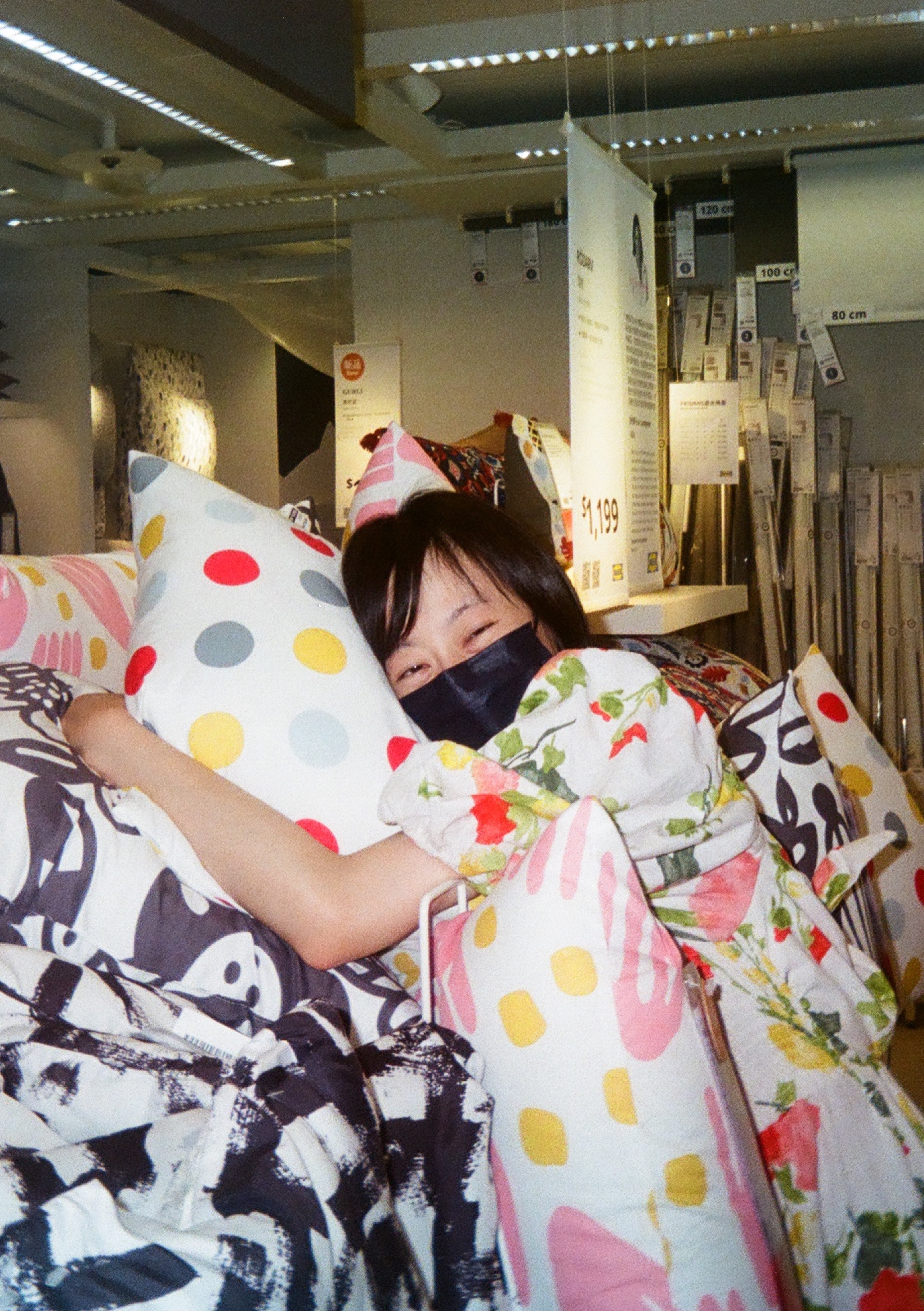 A woman wearing a mask hugging a pillow whose pattern matches the colors of her dress.
