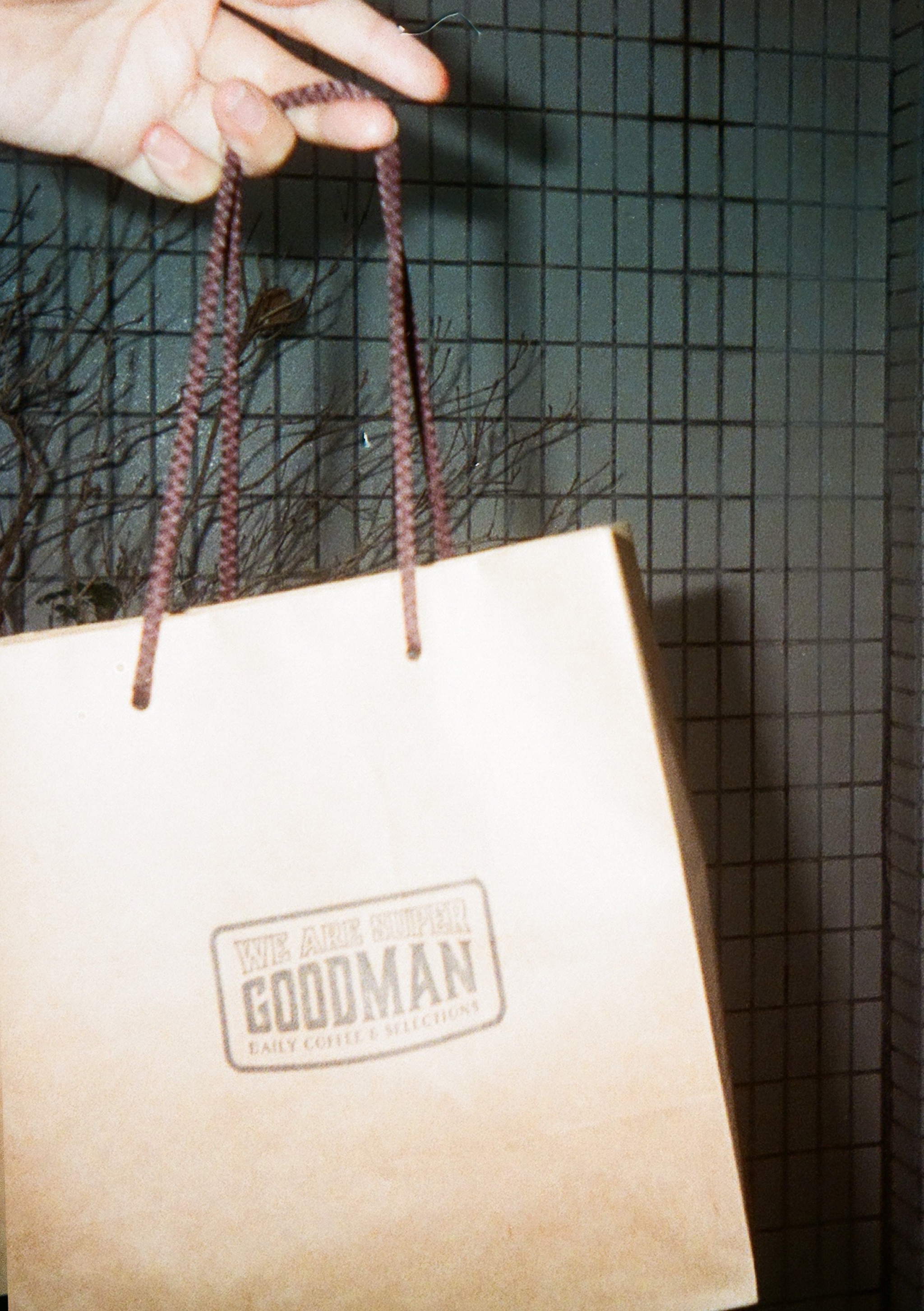 Hand holding a paper bag reading WE ARE SUPER GOODMAN, DAILY COFFEE & SELECTIONS.